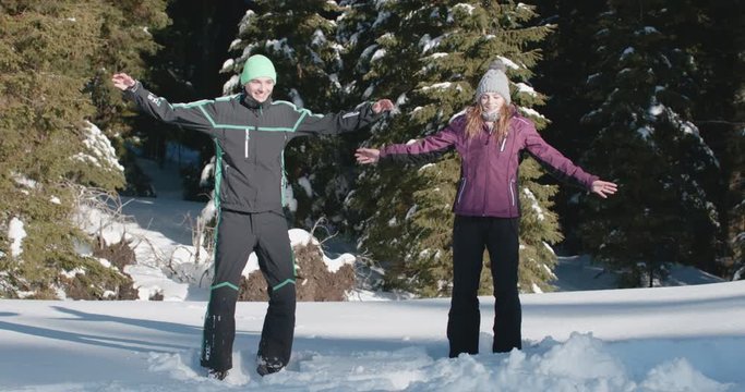 Young couple doing jumping jacks in the middle of a snowy forest on a beautiful, sunny day