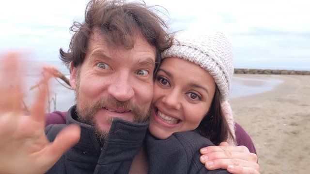 Funny couple shooting with camera playing doing selfie on beach in winter