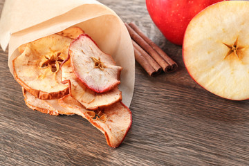 Tasty apple chips wrapped in paper on wooden table