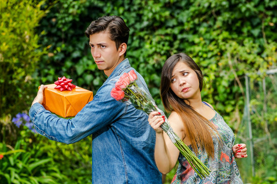 Close Up Of Mad Woman Holding Flowers And Mad Man Holding A Gift Back To Back Ignoring Each Other, Friend Zone Concept