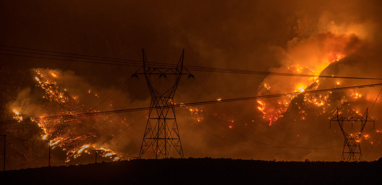 Large wildfire in California on hillside behind silhouette of powerlines