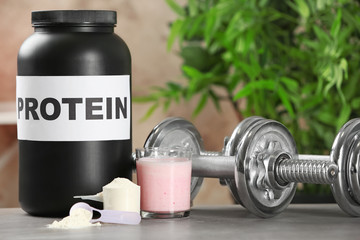 Composition with protein powder, shake and dumbbells on table