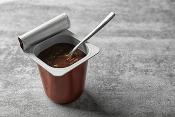 Plastic cup with chocolate yogurt on grey background