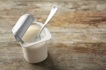 Gordijnen Plastic cup with yogurt on wooden background © Africa Studio