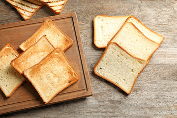 Wooden board with tasty toasted bread on table