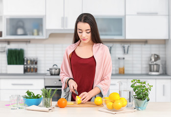 Young woman preparing tasty lemonade in kitchen