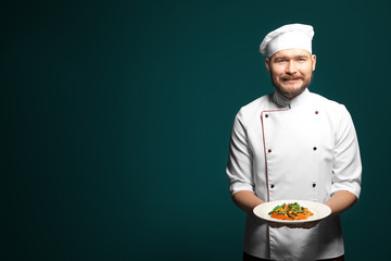 Handsome male chef holding plate with dish on color background