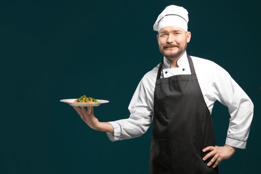 Handsome male chef holding plate with dish on color background