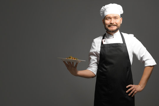 Handsome male chef holding plate with dish on dark background