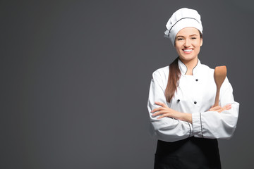 Beautiful female chef with wooden spoon on dark background
