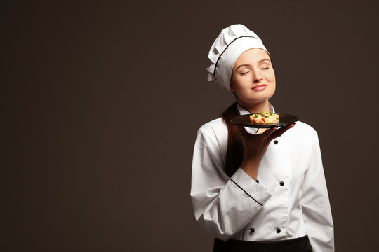 Beautiful female chef holding plate with dish on dark background