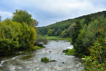 Countryside landscape with view of stormy river, slopes, glade and trees.