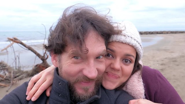 Funny couple shooting with camera selfie on beach in winter