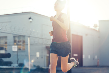 Obraz premium Woman athlete running at sunset at industrial city area