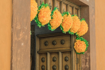 Seven large yellow paper flowers, around the top of a door frame, with a portion of a decorative wooden door in the background - 191125900