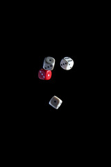 three white and one red dice on a black background during a free fall.