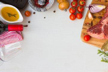 Frame of raw beef entrecote with tomato, olive oil, speases, red wine and frying pan. Top view with space for text.