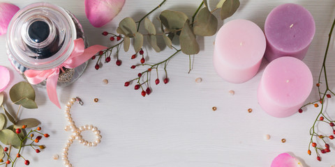 Frame of jar for cookies, pearl necklace and three pink candles on light background. Dogrose and branches of evkalipt.