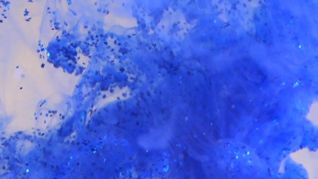 Colored Ink Dropped Into Water. Lovely bright metamorphosis. Cuttlefish ink splatter. volume effect. white background. blue dye with glitter in water. Slow motion.