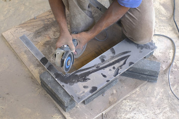 Worker cutting floor tiles with angle grinder at construction site