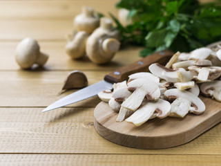 Fresh sliced mushrooms on chopping Board and parsley and knife on wooden table.