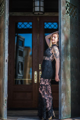 Rustic doors open to reveal alternative model in black lace evening gown leaning back as glass reflects blue sky.