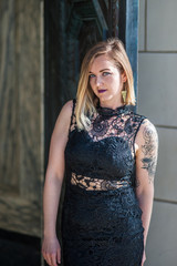 Young woman with tattoo arm waiting in black lace evening gown in doorway.