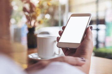 Mockup image of a woman's hand holding white mobile phone with blank desktop screen and coffee cup in cafe