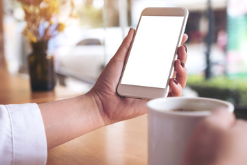 Mockup image of a woman's hand holding white mobile phone with blank desktop screen and coffee cup in cafe