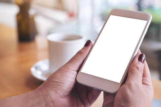 Mockup image of a woman's hand holding white mobile phone with blank desktop screen and coffee cup in cafe