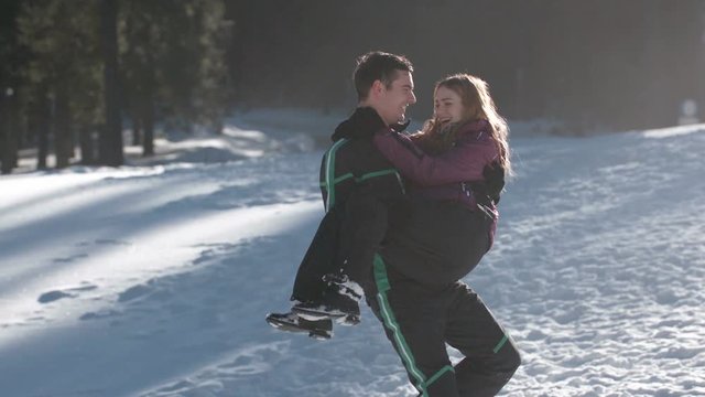 Young man carrying his parter in his arms before falling in high snow on a sunny day