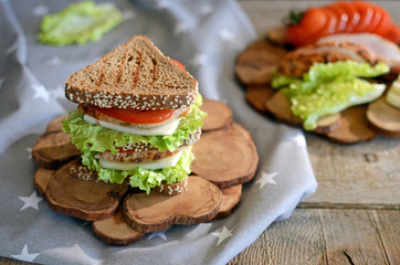 Sandwich of triangular bread with chicken breast tomato and cheese Wooden stand