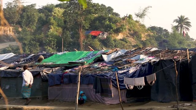 A man walks on a dirt road next to some small tin houses in a refugee camp