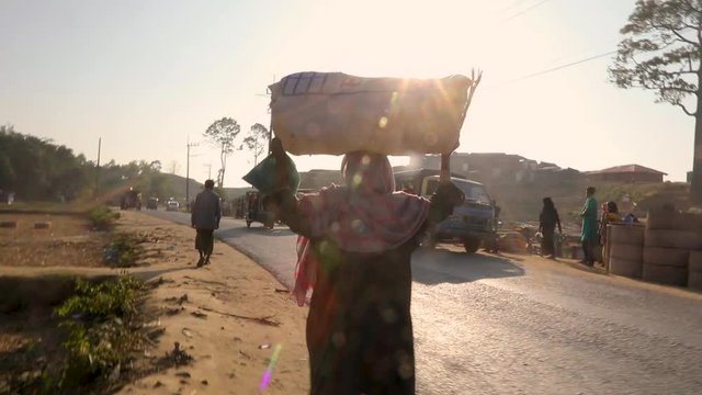 Camera follows a refugee woman carrying a wicker basket on her head