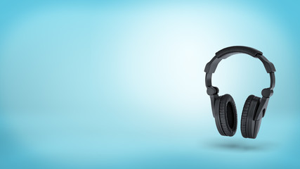 3d rendering of a large black wireless padded headphones in front view on blue background.