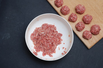 A Bowl with Minced Meat and Meatballs Isolated on Wooden board Over Dark Background. top View.