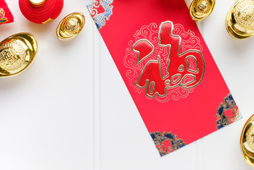 Top view Chinese New year red envelope packet (ang pow) with gold ingots on white wood table...