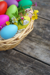 Fototapeta na wymiar Basket with colorful eggs and springtime flowers on wooden table