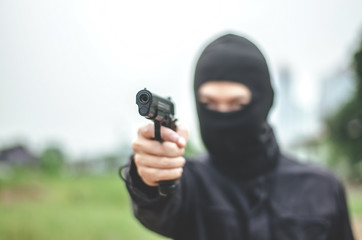 Mask thief in balaclava with holding gun ,Outlaw bad man  hold a gun pointing the target , robber in black hood holding gun and pointing to victim