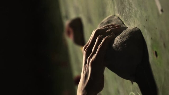 Close-up of a climber climbs on a stone wall indoors. The Sculpture. The hand is fixed at the finish. The exercise is completed.