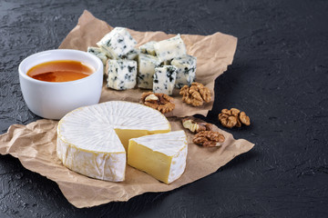 Camembert cheese, blue cheese, honey and walnuts on a dark background.