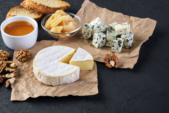 Cheese camembert, blue cheese, parmesan, toasts, honey and walnut on a dark background.