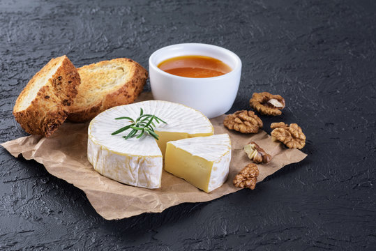 Camembert cheese, toasts, rosemary, honey and walnuts on a dark background.
