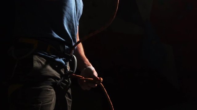 A crane of the hand of an athlete who ties up a climber's rope to climb a mountain on a black background. Slow motion.