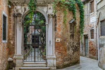 Old courtyard with ornate gate and narrow street in Venice Italy
