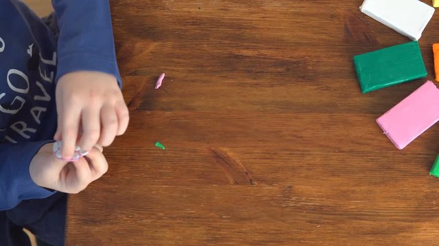 Cute little boy moulds from plasticine on table, top view