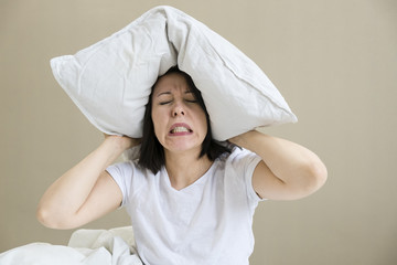 Bed Asian woman covering ears with pillow because of noise. Funny image isolated on white background.