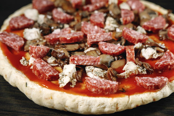 pizza cooking, meat of chiken, sausage salami, thick dough,  pizza crust, pizza is on a dark table, pizza with chicken and sausage salami, cooking process, mushrooms,  Champignon