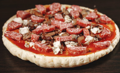 pizza cooking, meat of chiken, sausage salami, thick dough,  pizza crust, pizza is on a dark table, pizza with chicken and sausage salami, cooking process, mushrooms,  Champignon