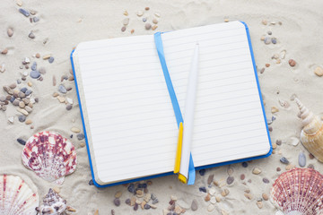 Enjoying vacation planning mood, notepad and sea shells on white sand background. Top view, closeup.